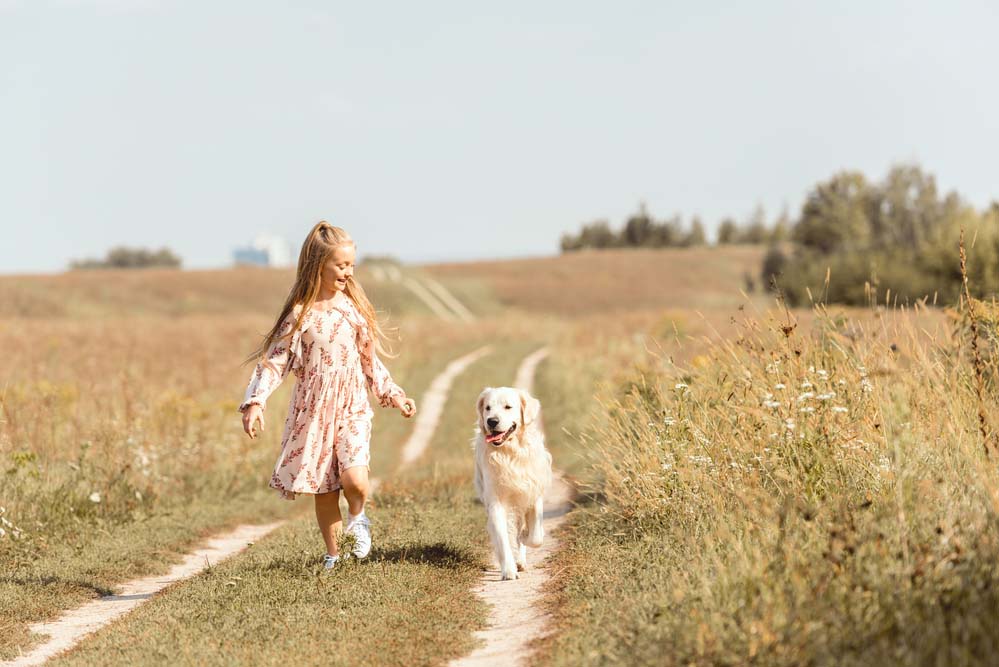 a child with a dog running down a path in a rural field